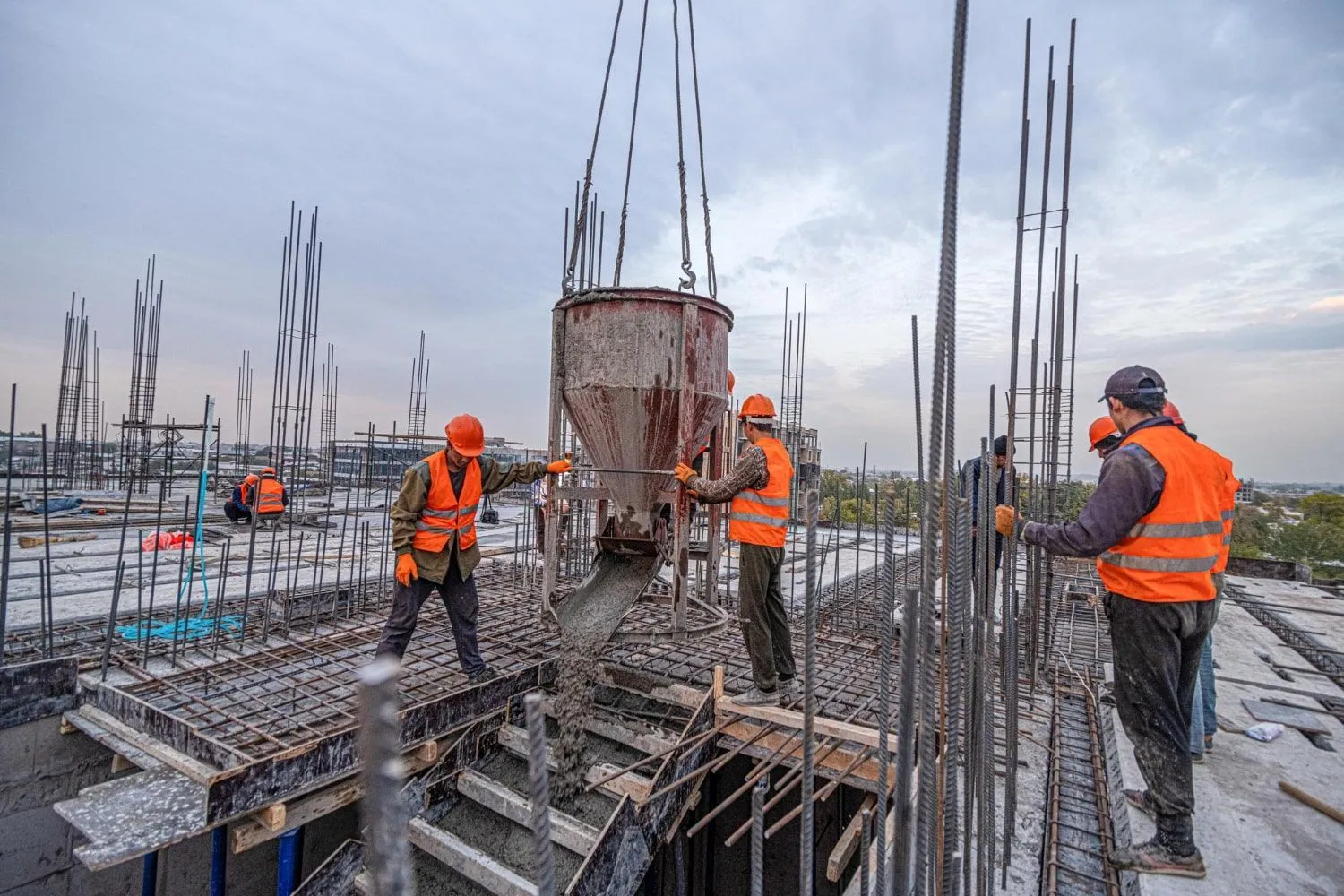 Crew guiding a crane-hung concrete bucket over rebar on a foundation deck