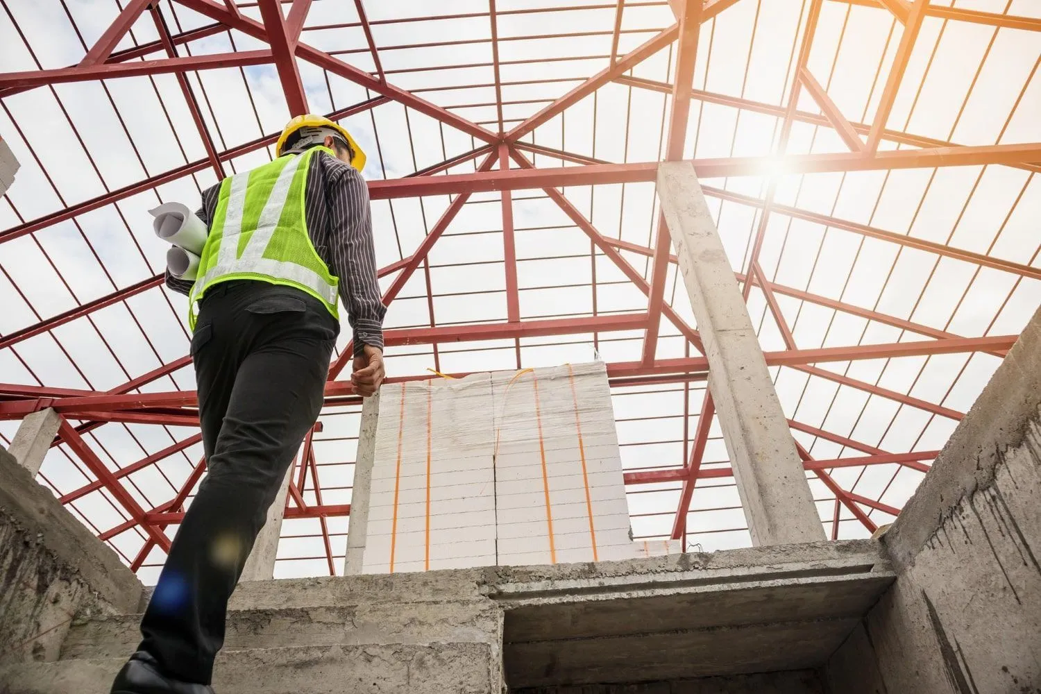 Worker in a hard hat and safety vest walking across a framed concrete structure